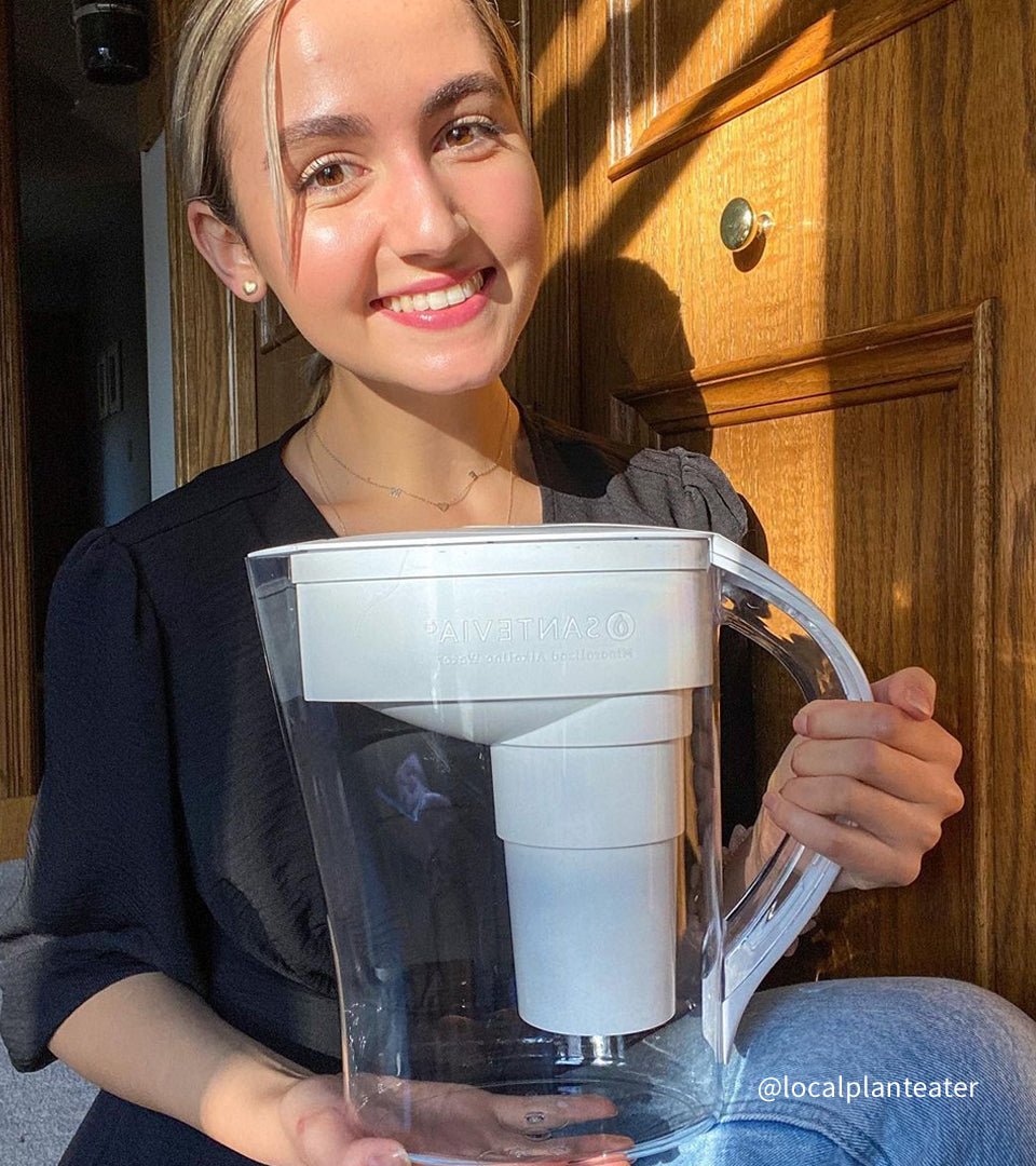 @localplanteater A woman sitting crossed legged smiling and holding her white Santevia MINA Alkaline Pitcher